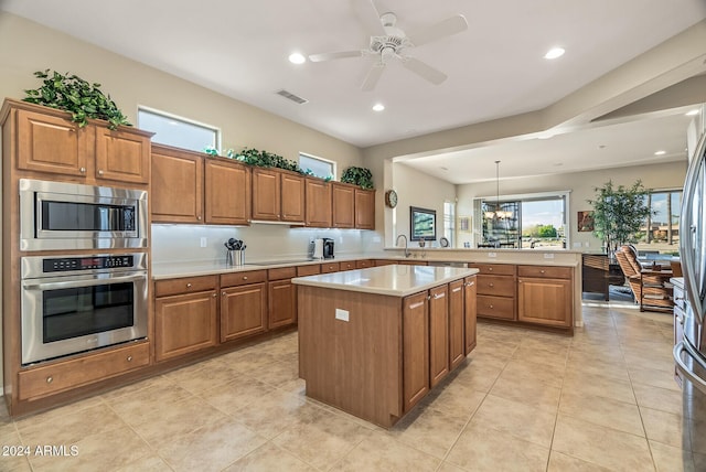 kitchen with a center island, ceiling fan with notable chandelier, decorative light fixtures, kitchen peninsula, and stainless steel appliances