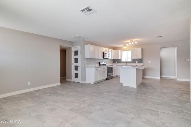 kitchen with tasteful backsplash, stainless steel appliances, light stone counters, a center island, and white cabinetry