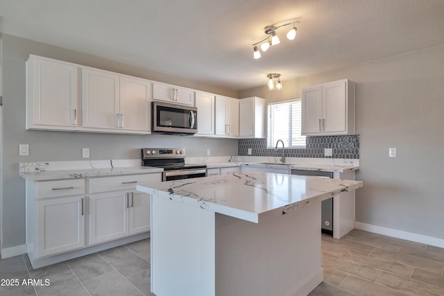 kitchen with appliances with stainless steel finishes, light stone counters, a center island, sink, and white cabinetry