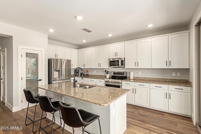 7858 W Fetlock Trl, Peoria, AZ 85383 - kitchen with stainless steel appliances, white cabinets, a breakfast bar area, a center island with sink, and wood finished floors