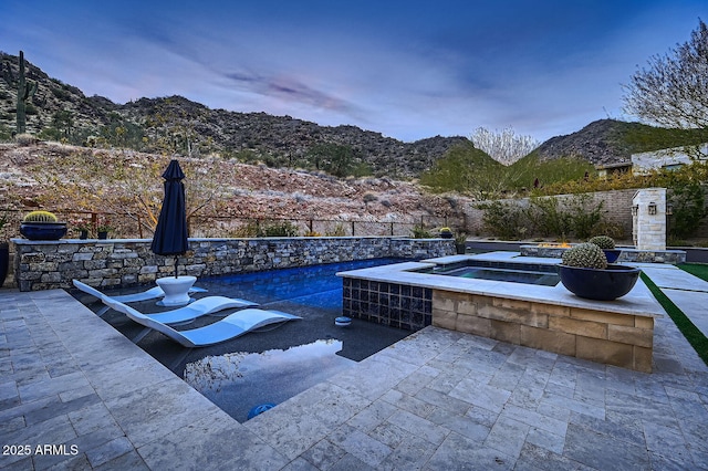 patio terrace at dusk featuring a swimming pool with hot tub and a mountain view