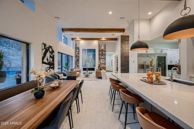 kitchen featuring stainless steel built in refrigerator, sink, light stone counters, decorative light fixtures, and a high ceiling