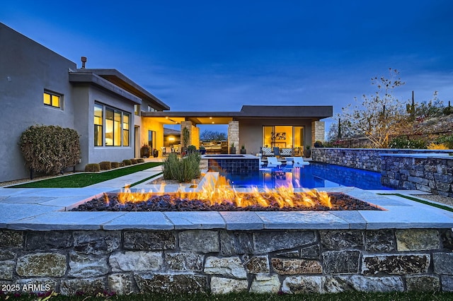 pool at dusk with a patio area and a fire pit