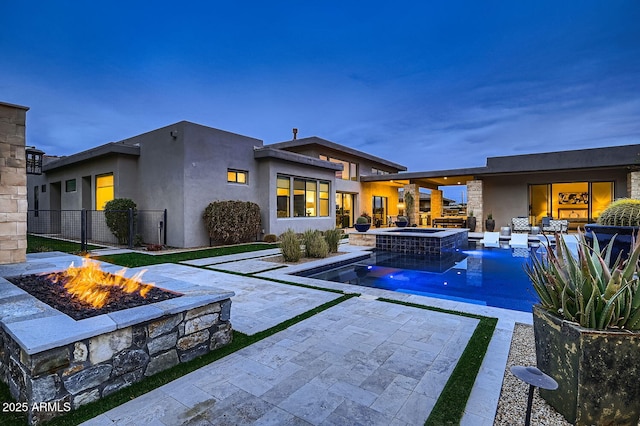 back house at dusk featuring a swimming pool with hot tub, a patio, and an outdoor fire pit