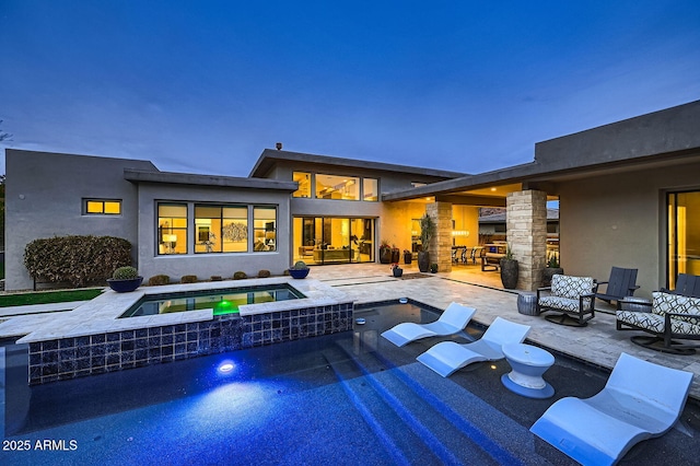 pool at dusk featuring an in ground hot tub, a fireplace, and a patio