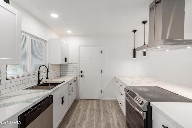 kitchen featuring sink, hanging light fixtures, wall chimney range hood, white cabinets, and appliances with stainless steel finishes