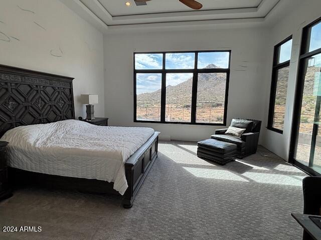 carpeted bedroom with a mountain view, access to outside, a raised ceiling, and ceiling fan