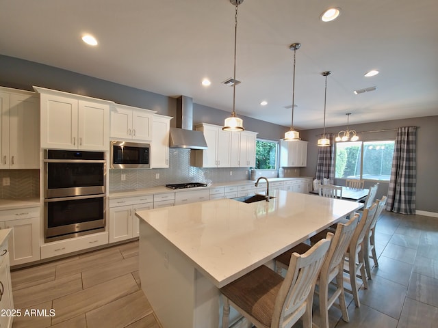 9187 W Parkside Ln, Peoria, AZ 85383 - kitchen with wall chimney range hood, stainless steel appliances, decorative backsplash, white cabinets, and a center island with sink