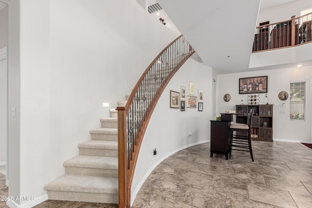 staircase featuring baseboards, a high ceiling, and stone finish flooring