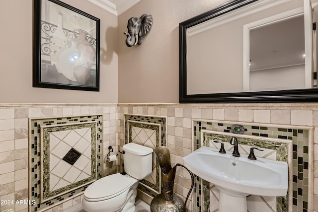 half bath with crown molding, toilet, wainscoting, tile walls, and a sink