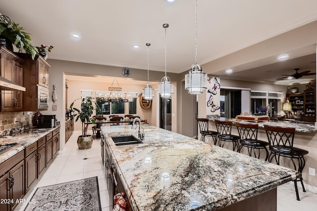 kitchen featuring a large island with sink, ceiling fan, decorative backsplash, a sink, and stainless steel microwave