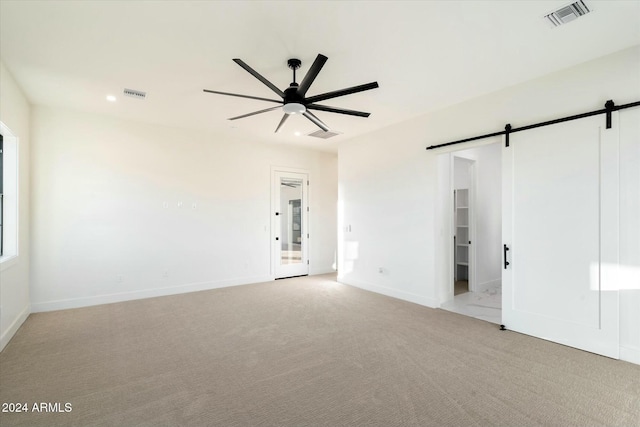 unfurnished room featuring a barn door, a ceiling fan, visible vents, and light colored carpet