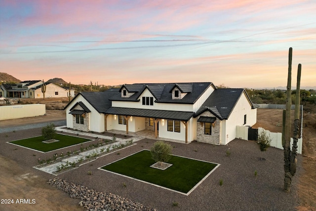 modern farmhouse featuring stucco siding, fence, metal roof, stone siding, and driveway