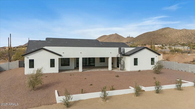 rear view of house with stucco siding, a fenced backyard, a mountain view, and a patio