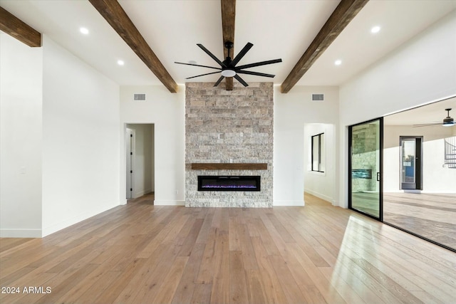 unfurnished living room featuring ceiling fan, a stone fireplace, baseboards, light wood finished floors, and beamed ceiling