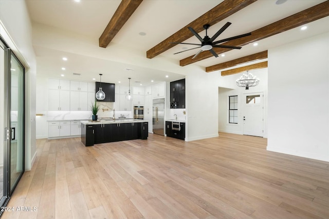 kitchen with light wood finished floors, appliances with stainless steel finishes, light countertops, dark cabinetry, and a large island with sink