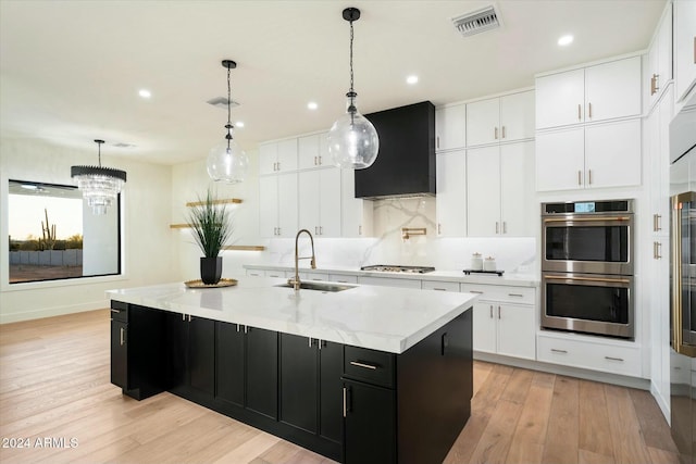 kitchen with a sink, wall chimney range hood, appliances with stainless steel finishes, dark cabinetry, and tasteful backsplash