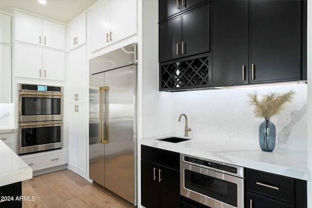 kitchen with tasteful backsplash, appliances with stainless steel finishes, dark cabinetry, white cabinetry, and a sink