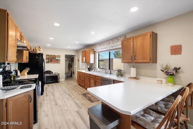 kitchen featuring black stove, under cabinet range hood, a kitchen bar, light countertops, and a peninsula