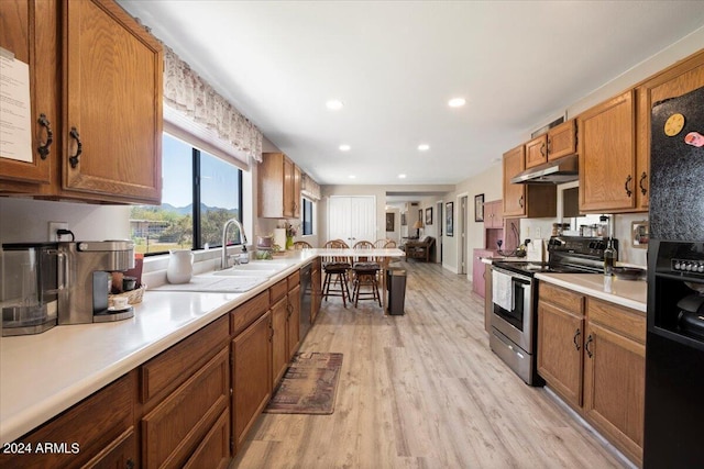 kitchen featuring a sink, black appliances, light countertops, under cabinet range hood, and brown cabinets