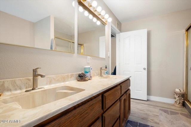 bathroom featuring double vanity, baseboards, a shower with shower door, and a sink