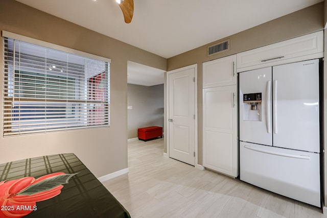 kitchen featuring ceiling fan, white fridge with ice dispenser, and white cabinetry