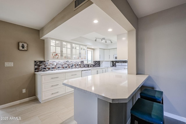 kitchen with kitchen peninsula, decorative backsplash, white appliances, white cabinetry, and a breakfast bar area