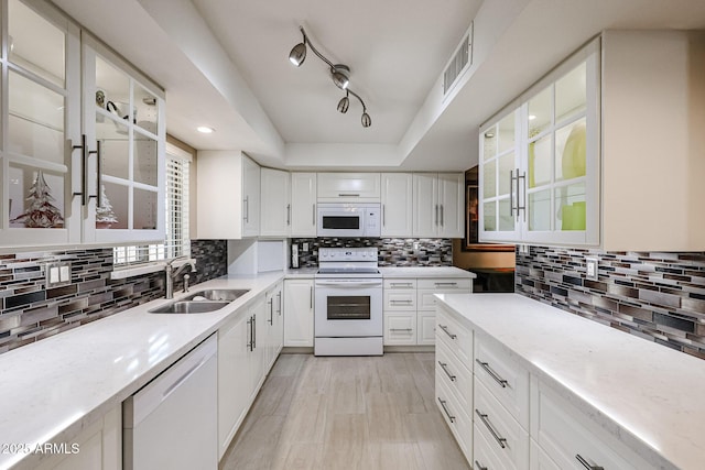 kitchen featuring white appliances, white cabinets, decorative backsplash, sink, and a tray ceiling