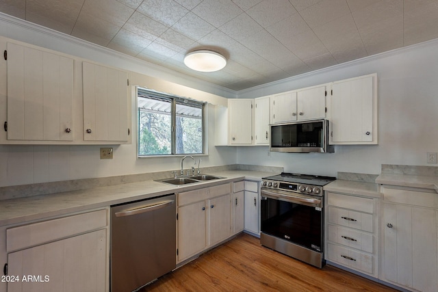 kitchen with light wood finished floors, white cabinets, stainless steel appliances, light countertops, and a sink