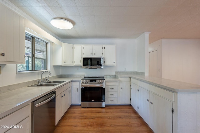 kitchen with white cabinets, a peninsula, stainless steel appliances, light countertops, and a sink