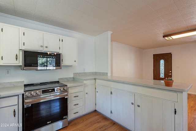 kitchen with light wood-style flooring, a peninsula, white cabinetry, light countertops, and appliances with stainless steel finishes