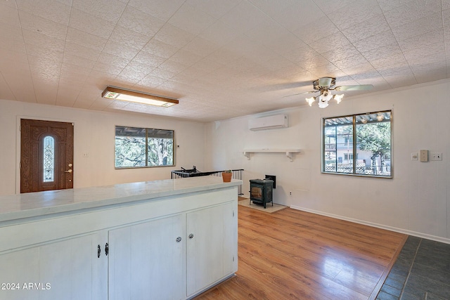 kitchen featuring light countertops, light wood-style floors, a wood stove, white cabinets, and a wall mounted air conditioner