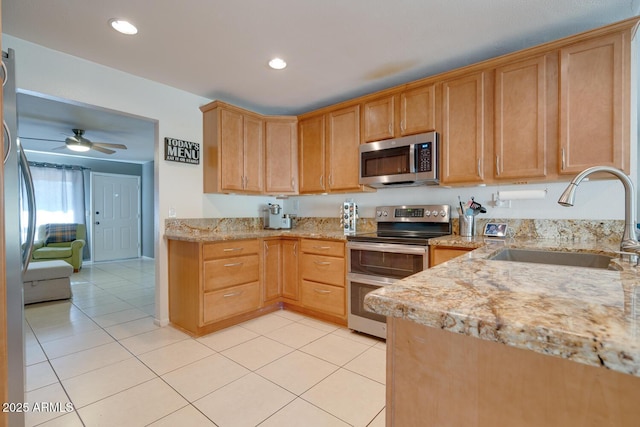 kitchen with sink, light tile patterned floors, appliances with stainless steel finishes, ceiling fan, and light stone countertops