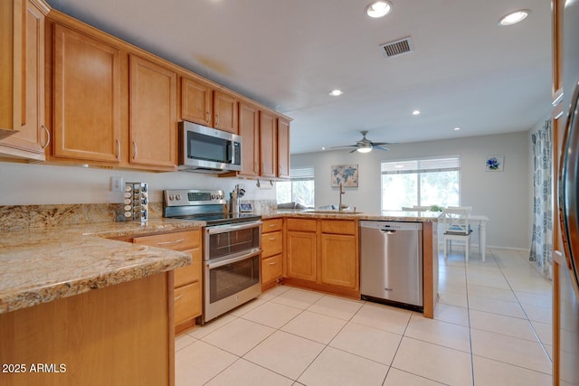 kitchen with sink, stainless steel appliances, light stone counters, light tile patterned flooring, and kitchen peninsula