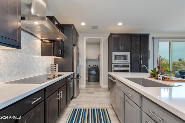 kitchen featuring tasteful backsplash, wall chimney exhaust hood, stainless steel appliances, sink, and light hardwood / wood-style flooring