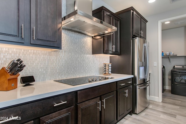 kitchen featuring black electric stovetop, wall chimney range hood, light hardwood / wood-style flooring, independent washer and dryer, and tasteful backsplash