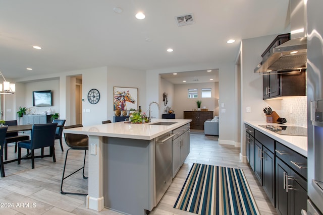 kitchen featuring black electric cooktop, wall chimney range hood, sink, light hardwood / wood-style floors, and an island with sink