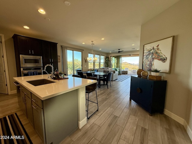 kitchen featuring a kitchen island with sink, ceiling fan with notable chandelier, sink, light hardwood / wood-style flooring, and appliances with stainless steel finishes