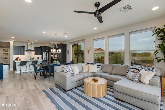 living room featuring light hardwood / wood-style flooring, ceiling fan with notable chandelier, and sink