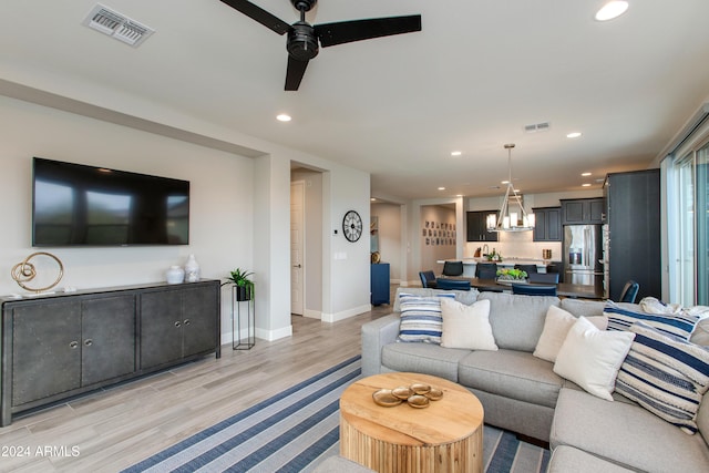 living room with ceiling fan with notable chandelier and light wood-type flooring