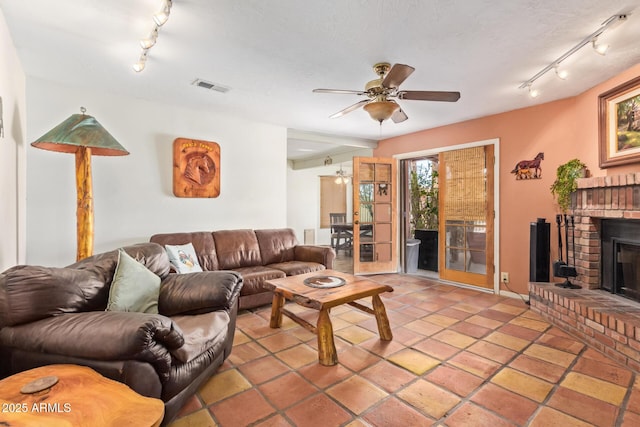 tiled living room with a brick fireplace, track lighting, visible vents, and a ceiling fan