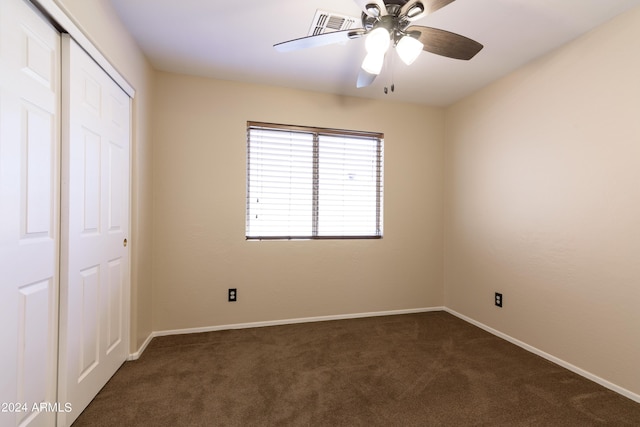 unfurnished bedroom with dark colored carpet, a closet, and ceiling fan