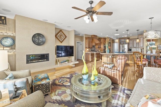 living room with ceiling fan, sink, and light wood-type flooring