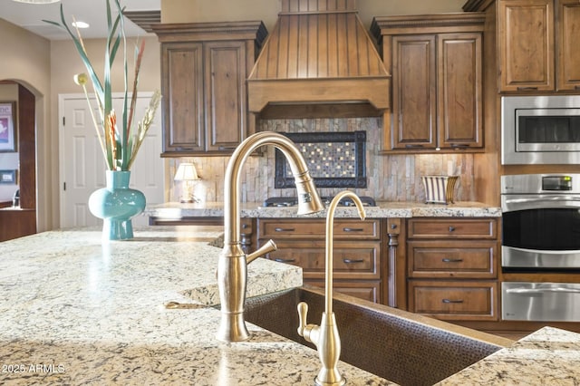 kitchen with stainless steel appliances, tasteful backsplash, custom range hood, and light stone counters