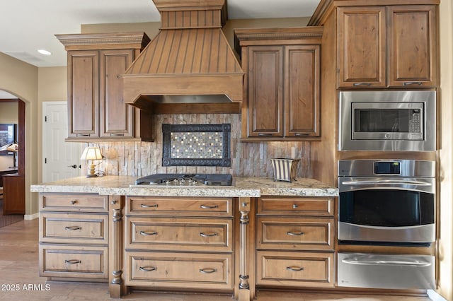 kitchen featuring light stone countertops, appliances with stainless steel finishes, custom range hood, and backsplash