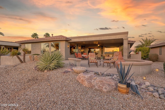 back house at dusk with ceiling fan and a patio area