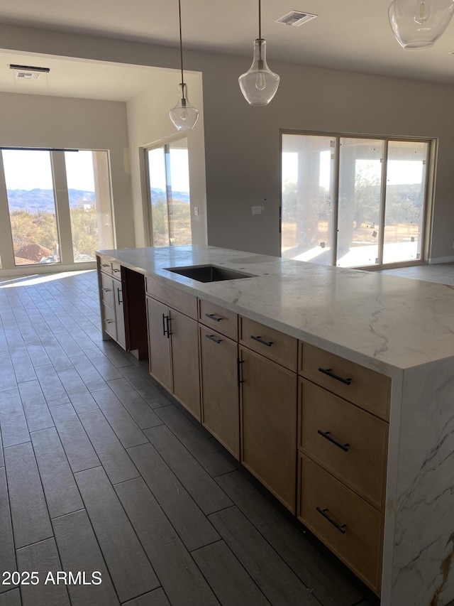 kitchen with sink, light brown cabinetry, hanging light fixtures, and light stone counters