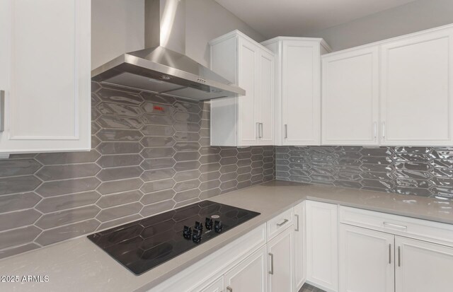 kitchen with wall chimney exhaust hood, tasteful backsplash, white cabinetry, black electric stovetop, and light countertops