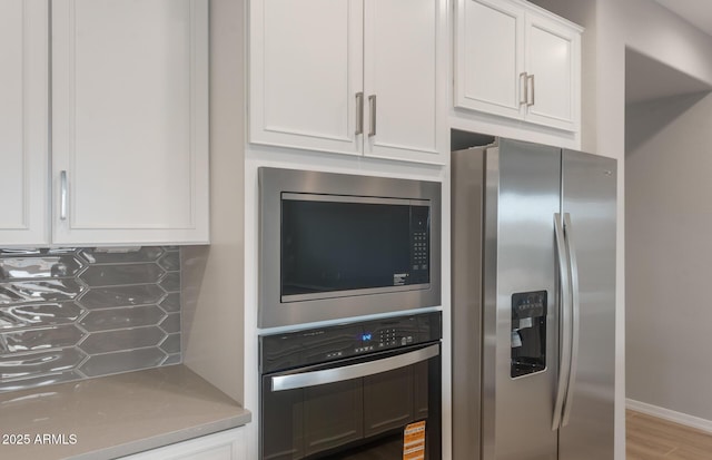 kitchen featuring white cabinets, backsplash, wood finished floors, light countertops, and appliances with stainless steel finishes