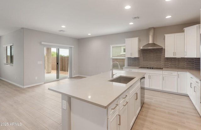 kitchen with light wood finished floors, visible vents, wall chimney range hood, a sink, and black electric stovetop